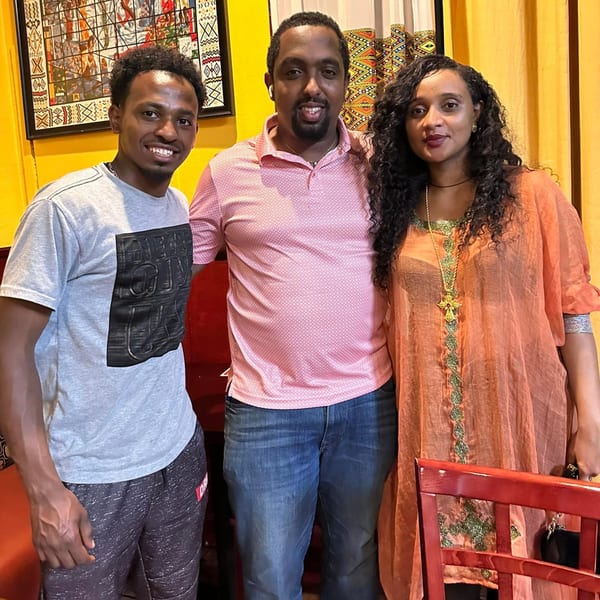 Three smiling people, two men and one woman, standing together in an Ethiopian restaurant.
