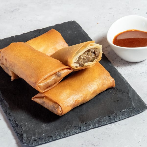 Crispy Ethiopian spring rolls with savory meat filling, one cut open, served with dipping sauce.