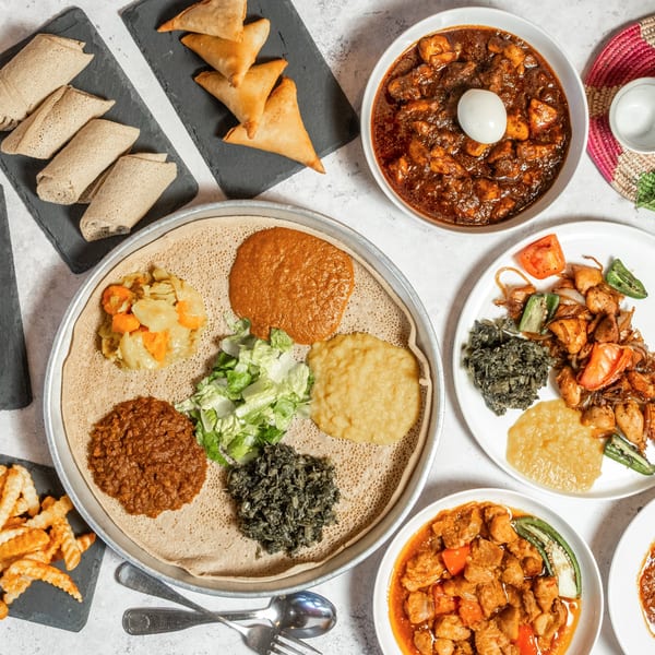 An overhead shot of a large spread of Ethiopian dishes, including injera, stews, and sambusas.