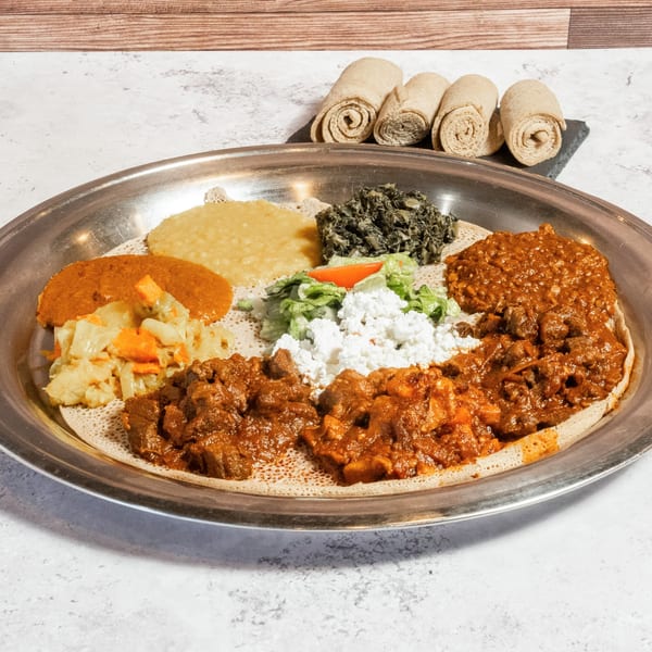 A large platter of Ethiopian food, including various stews, vegetables, and injera bread.