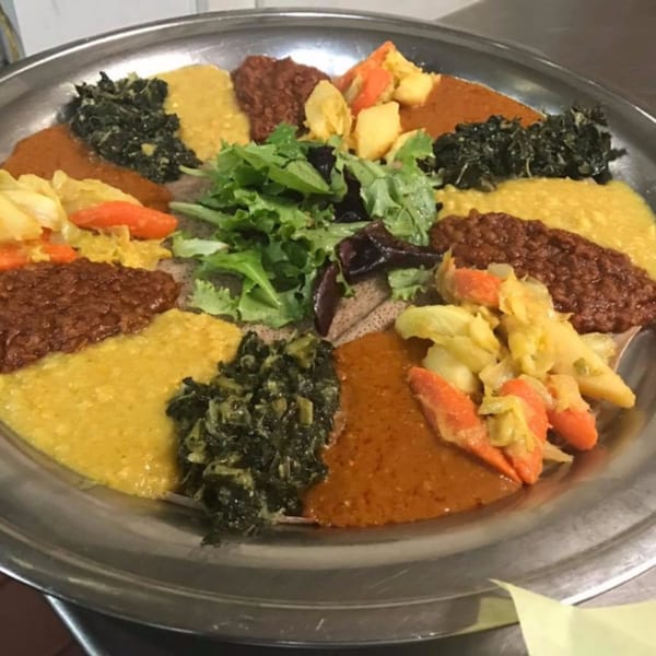 A large platter of Ethiopian injera bread topped with various colorful stews, vegetables, and lentils.