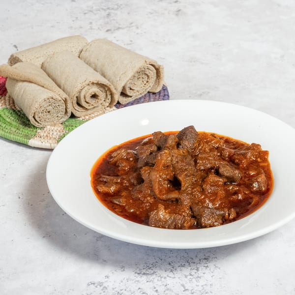 Walia Ethiopian Cuisine's red stew with meat chunks in a white bowl, with rolled injera bread.
