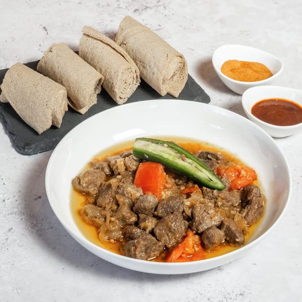 Ethiopian beef tibs with injera bread, a green pepper, and two small bowls of sauces.