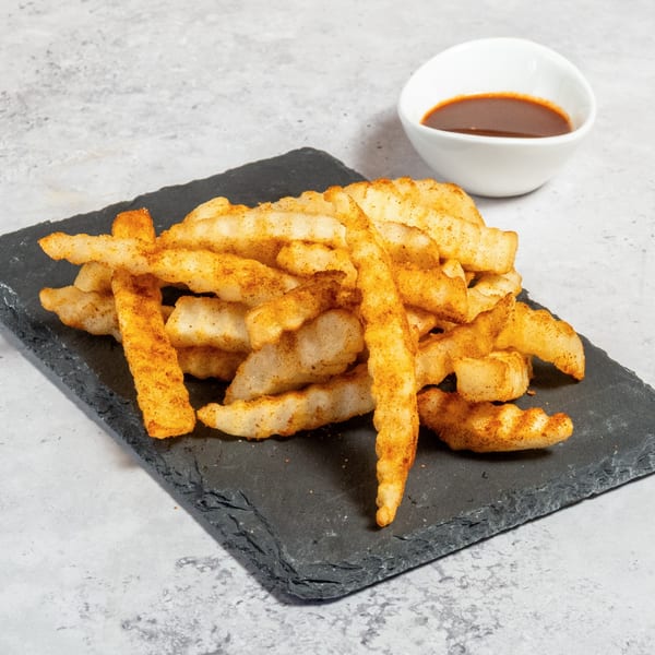 Seasoned crinkle-cut fries piled on a dark slate board with a side of dipping sauce.