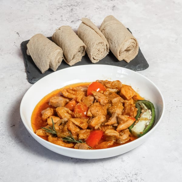 Walia Ethiopian Cuisine's Doro Wat, a chicken stew with injera bread rolls on a dark slate.