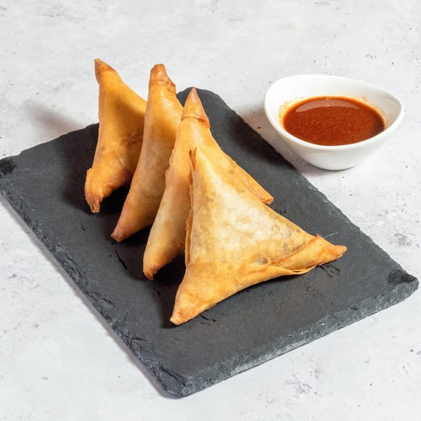 Three golden-brown Ethiopian sambusas on a dark slate board with a side of red dipping sauce.