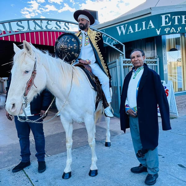 Man in traditional Ethiopian attire on a white horse, another man standing beside Walia Ethiopian Cuisine.